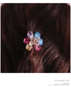 Detail shot of a small metal flower hair claw clip featuring colorful rhinestone crystal petals.
