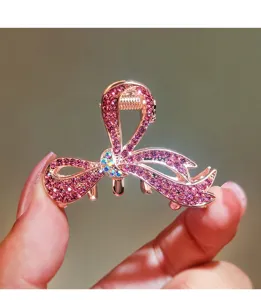 Detailed shot of a rose gold rhinestone bow hair claw clip, sparkling pink crystal details.