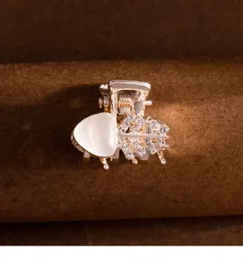 Vue détaillée d'une petite pince à cheveux dorée avec pierre blanche et feuilles de strass.