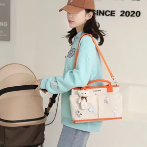 Large capacity canvas diaper bag with cute bear charm and orange straps for modern moms.