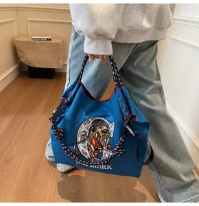 Detailed view of blue canvas tote bag with embroidered lion graphic and rope handles.
