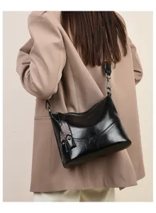 Detail shot of a black leather bucket bag worn on shoulder with wide strap and retro charm.