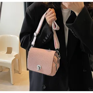 Close-up of stylish pink woven crossbody bag with metallic lock closure and wide patterned strap.