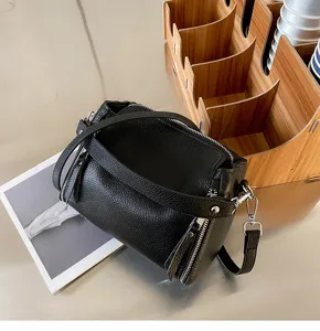 Detailed shot of black leather crossbody bag, showing geometric stitching and metal zipper hardware.