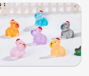 Close-up detail of cute luminous capybara resin charms with Christmas hats in a snow scene.