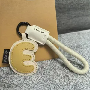 Detailed shot of leather letter keychain charm, two-tone design with braided strap and metal ring.