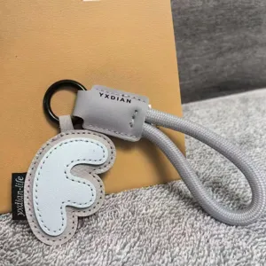 Close-up detail of grey leather keychain with letter pendant and braided rope strap gift.