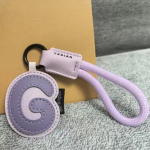 Close-up of a light purple leather letter G keychain pendant with a matching braided strap.