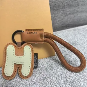 Leather letter H keychain detail shot, brown braided rope and PU leather bag charm accessory.