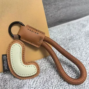 Close-up detail of the leather letter keychain pendant with braided rope and metal ring.