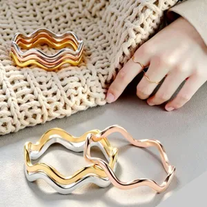 Primo piano dettagliato di bracciali e anelli metallici ondulati in argento, oro e oro rosa.