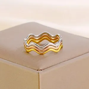 Primo piano dettagliato di tre anelli ondulati impilabili in argento, oro e oro rosa.