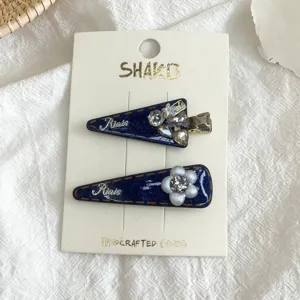 Detail view of blue denim triangle hair clips featuring sparkly rhinestones and floral pearl accents.