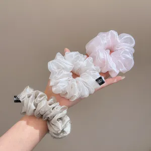 Detailed close-up showing pearlescent organza scrunchies in three soft pastel colors.