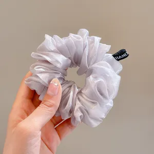 Detail view of a shimmering translucent organza hair scrunchie in light grey with a small tag.