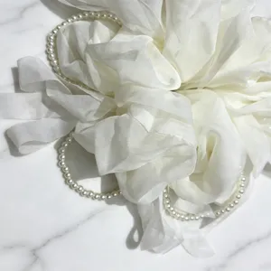 Gros plan détaillé du chouchou en tulle blanc avec chaînes de perles élégantes, douce texture.