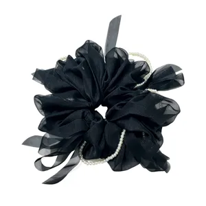 Gros plan detail de chouchou en organza noir avec chaine de perles et ruban elegant.