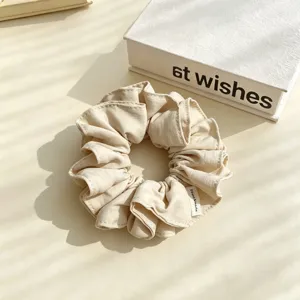 Beige fabric hair scrunchie detail view, soft ruffled ponytail holder fashion accessory.