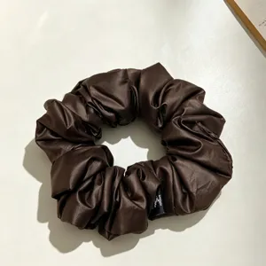 Vue détaillée de l'élégant chouchou en satin marron foncé, texture plissée délicate.