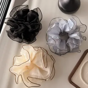 Close-up detail of three elegant organza hair scrunchies in black, grey, and beige colors.