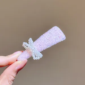 Detailopname van een sprankelende strass en parel strik haarcip in zachte lila tint.