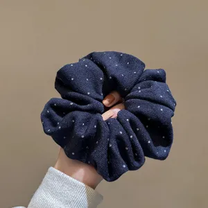 Detailed shot of dark blue fabric hair scrunchie with white polka dots, pleated elastic hair tie.