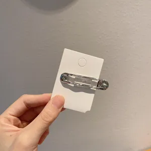 Gedetailleerde close-up van een moderne zilveren haarspeld op een witte displaykaart.