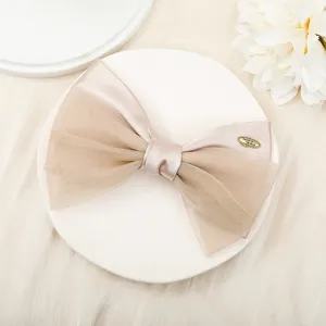 Close-up detail of champagne organza and satin double bow hair clip with metal tag accent.