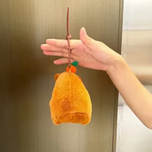 Détail de peluche capybara montrant sa queue à tirer et son chapeau d'orange.