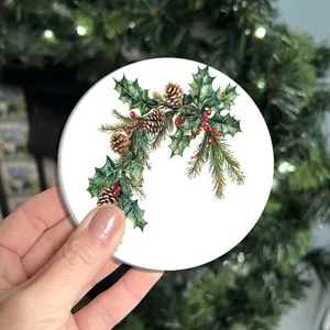 Close-up detail van een ronde kerstonderzetter met feestelijke hulst- en dennenappelillustratie.