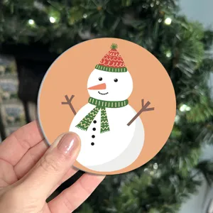 Close-up shot of a cute cartoon snowman car coaster with festive Christmas tree background.