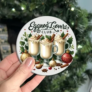 Close-up of a round vintage Christmas eggnog themed coaster held by hand with tree background.