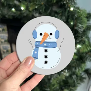 Close-up detail shot of a cute cartoon snowman car coaster with blue earmuffs and scarf.