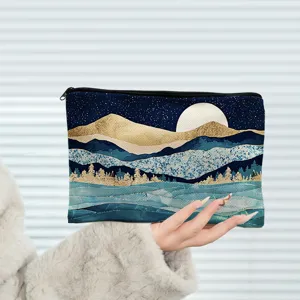 Détail de trousse de maquillage imprimé paysage de montagne bleu et or avec fermeture éclair.