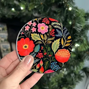 Round car cup coaster featuring vibrant folk floral pattern on black background, detail shot.