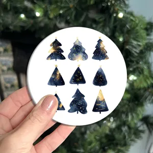 Detalle de mano sosteniendo posavasos navideño redondo con árboles de acuarela azul y oro
