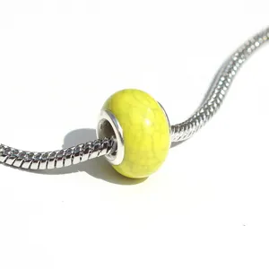 Gros plan détail d'une perle charm en pierre craquelée jaune vif sur un bracelet chaîne argent.