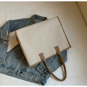 Vue détaillée du sac cabas en toile élégant avec bordure marron posé sur une veste en jean.