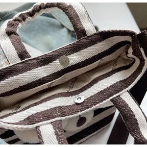 Close-up detail of brown and white striped canvas tote bag with snap button and handles.