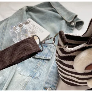 Brown striped canvas shoulder bag with wide strap and cute plush charm for women.