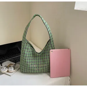 Green plaid shoulder bag detail showing textured tweed fabric and embroidered text design.