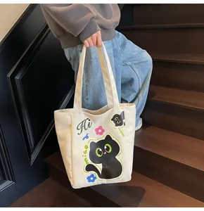 Vue détaillée du sac cabas en toile avec un adorable imprimé de chat noir et des bretelles.