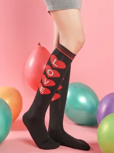 Close-up of black over-the-knee socks with red heart and love print for party wear.