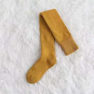 Detailaufnahme von kuscheligen gelben Overknee-Strümpfen flach auf weißem flauschigem Teppich.