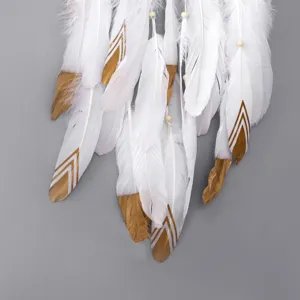 Detalle de pluma blanca artesanal con patrones geométricos dorados y cuentas de madera.