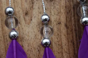 Close-up detail of handmade purple feather car hanging pendant with beads, rustic style.