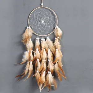 Detail shot of bohemian dream catcher with feathers and beads hanging on grey wall decoration.