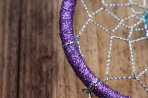 Close-up detail of purple dreamcatcher hoop wrapped with shiny thread and silver web.