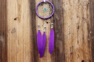 Handmade purple dream catcher hanging ornament with feathers for car decor or home wall.