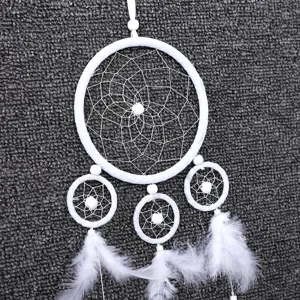 White handmade dream catcher detail shot featuring delicate feather and bead hanging decor.